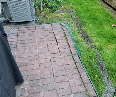 Worker applying lawn fertilizer with a broadcast spreader along a driveway